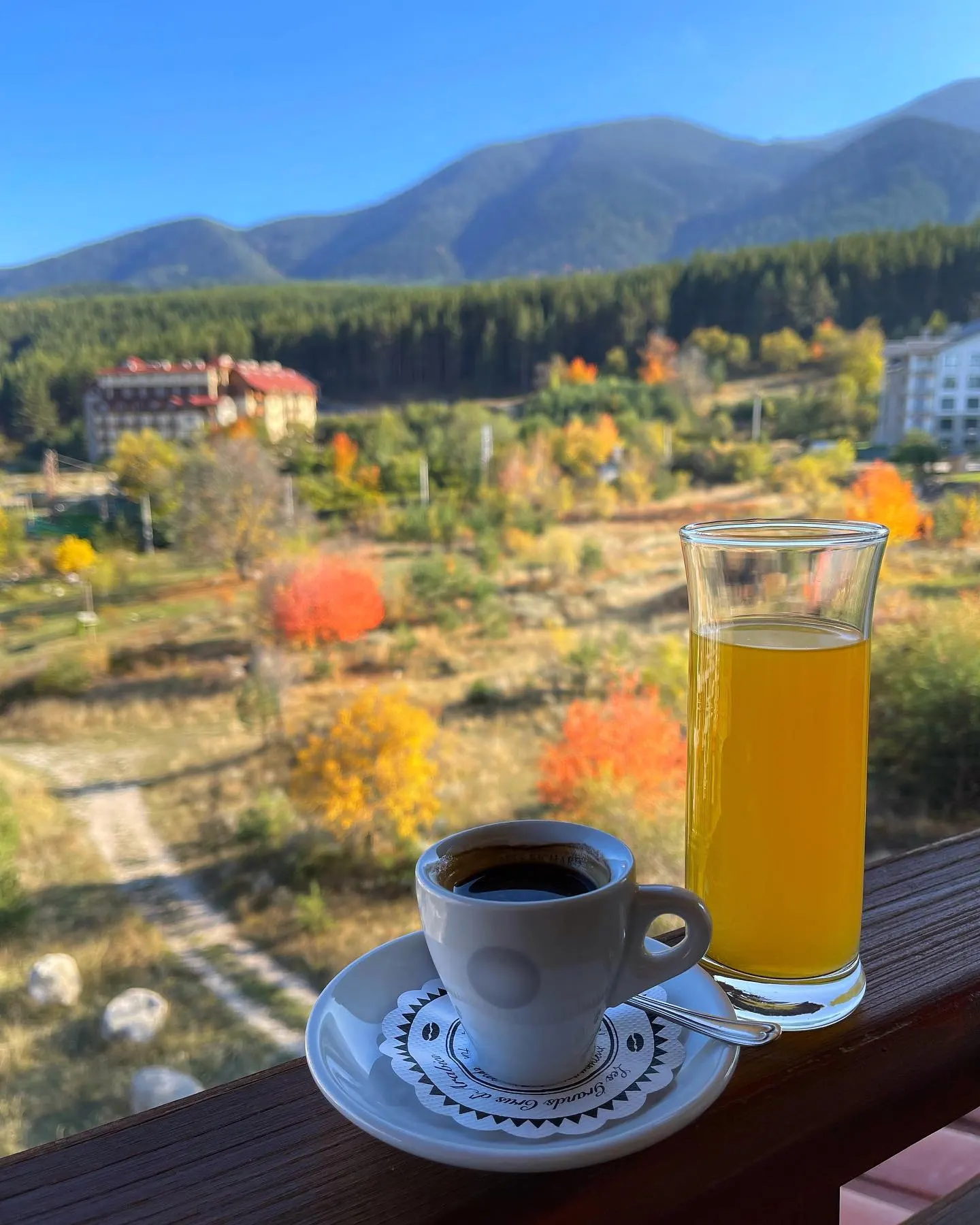 Coffee and orange juice on the balcony rail, with an autumn view over Bansko and the mountain