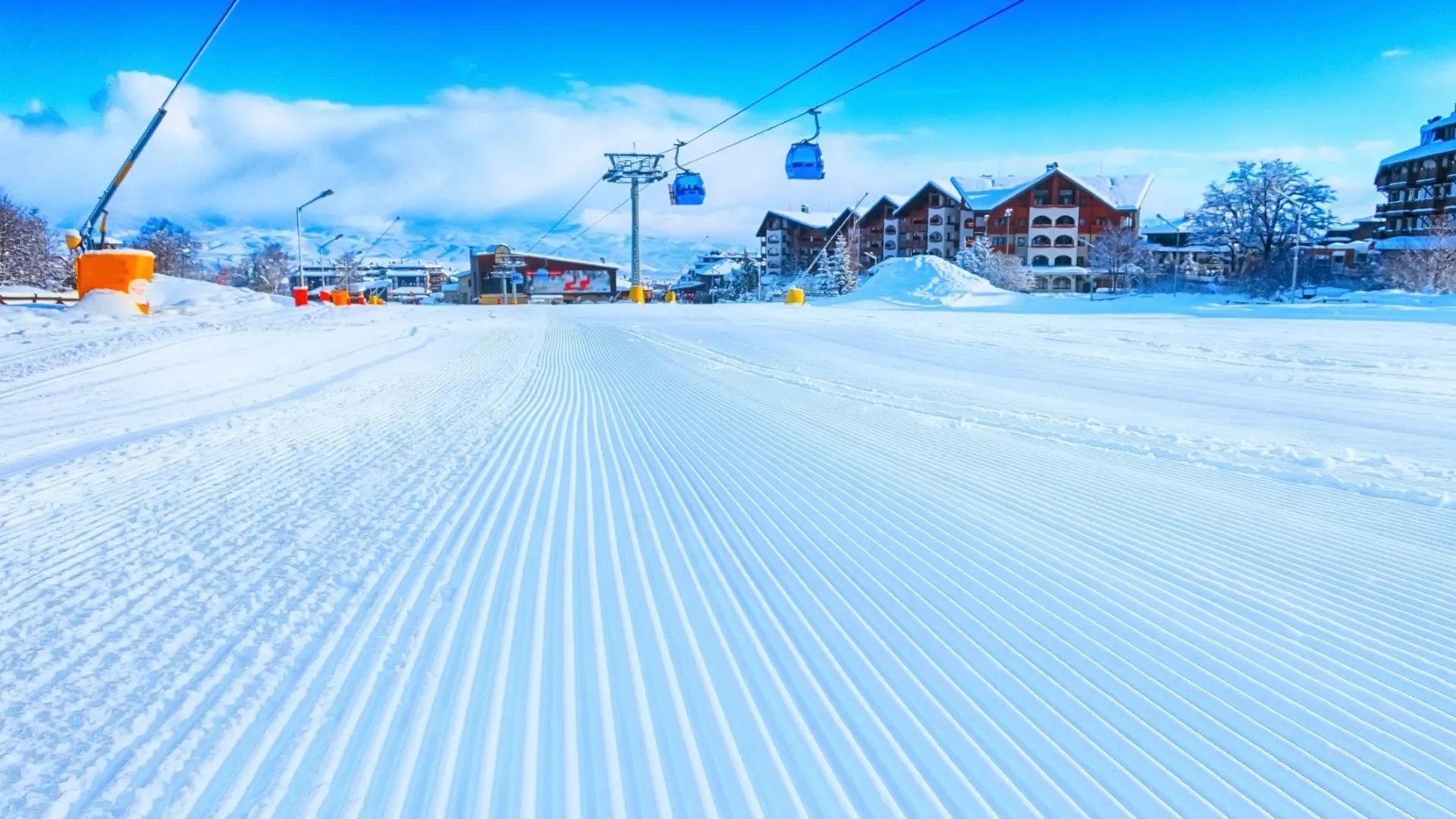A freshly groomed piste in Bansko, gondola cabins and hotels under a blue sky