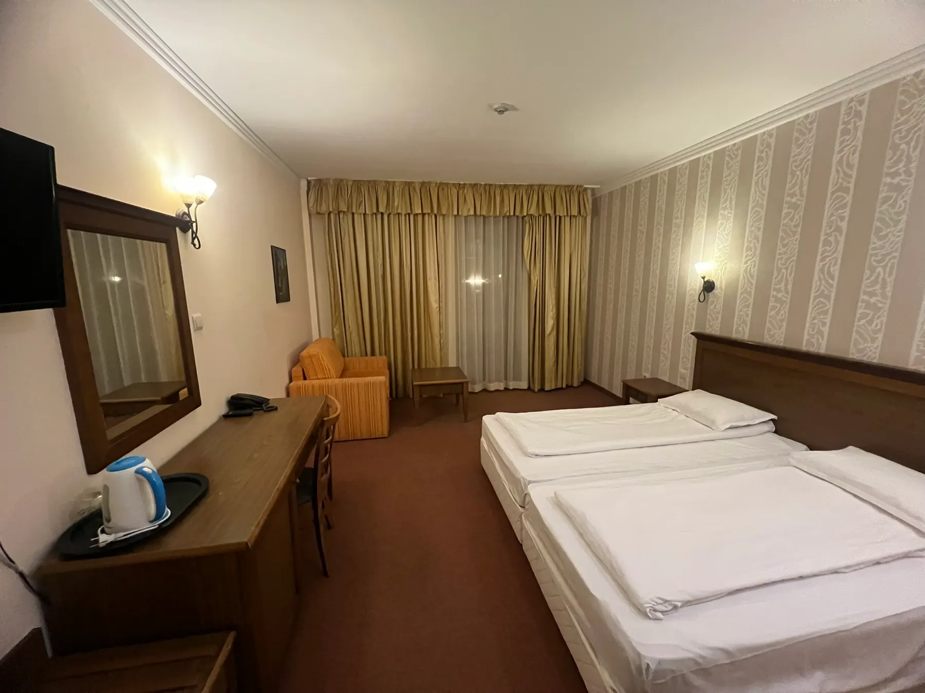 Deluxe room — television, a desk with a kettle, an armchair and the beds towards the window