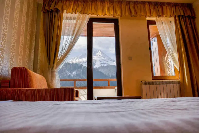 A room at the hotel — bed, armchair and a balcony door looking onto a snow-covered Pirin peak
